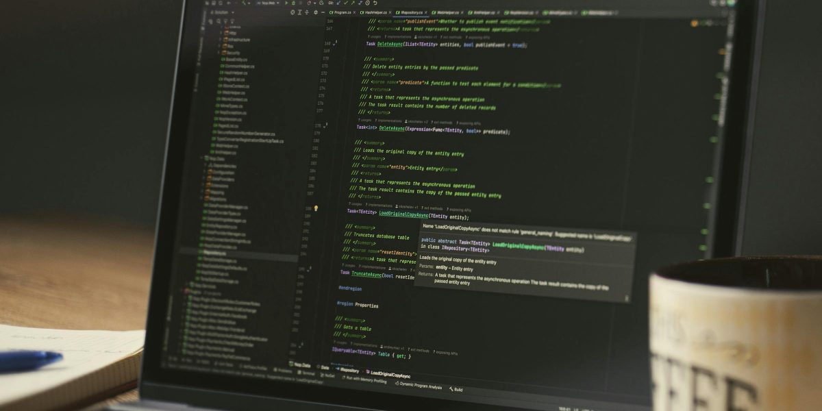 A close-up of a laptop displaying code in a dimly lit room with a coffee mug nearby.
