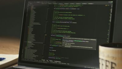A close-up of a laptop displaying code in a dimly lit room with a coffee mug nearby.