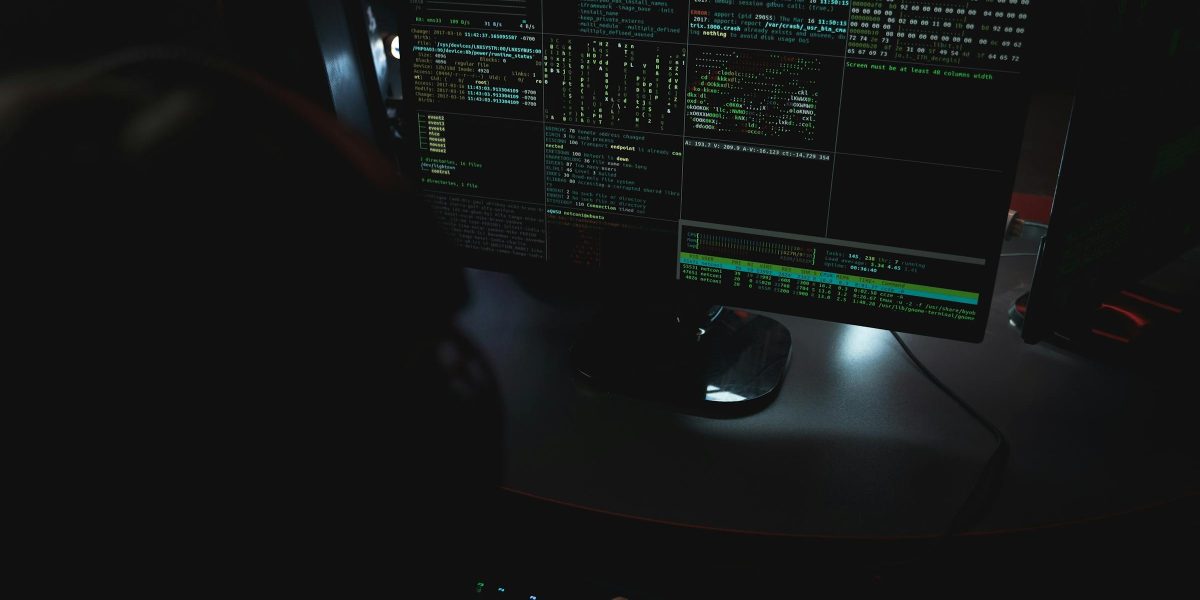 Dark room setup with code displayed on PC monitors highlighting cybersecurity themes.