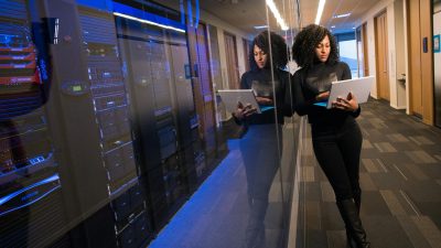 A woman using a laptop navigating a contemporary data center with mirrored servers.