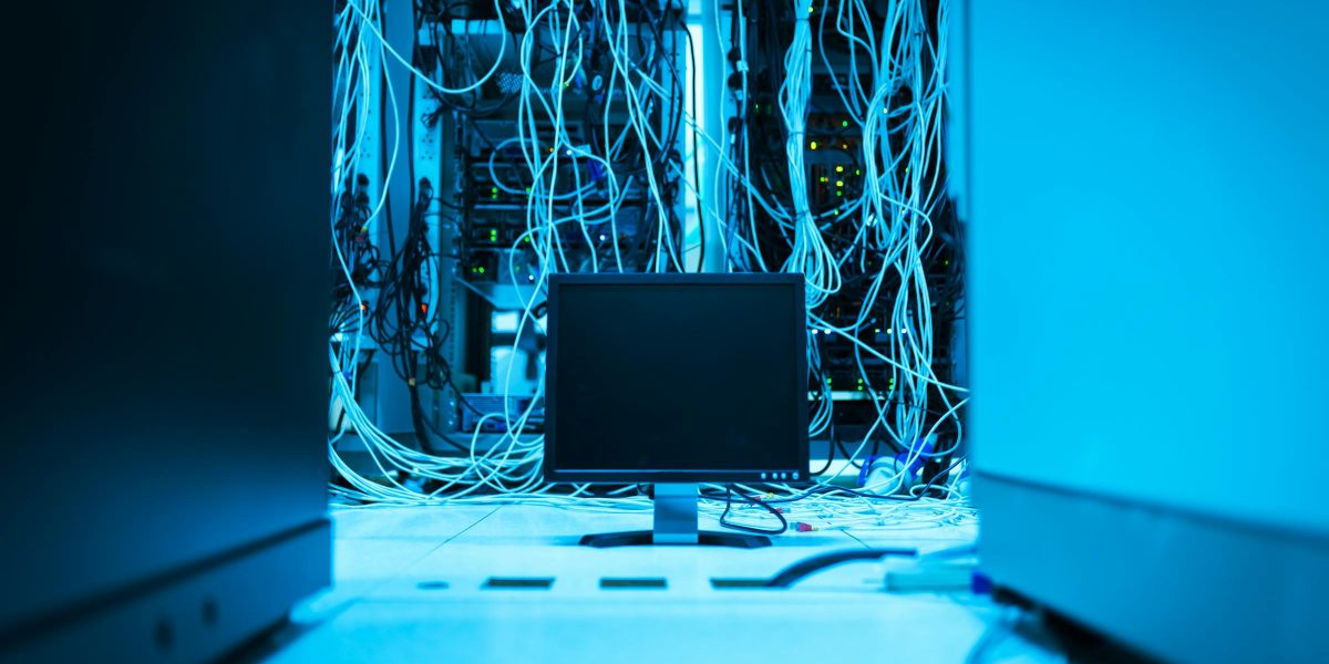 A complex network of cables in a data center with a monitor in the foreground.