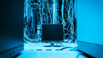 A complex network of cables in a data center with a monitor in the foreground.