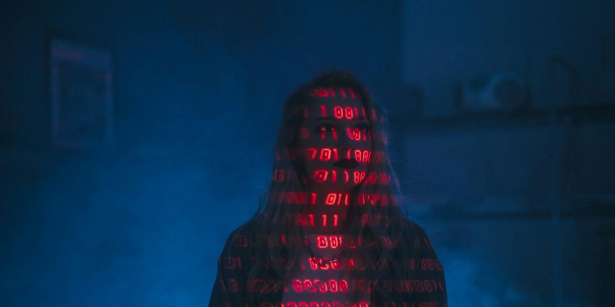 A mysterious silhouette with red binary code projected over the face, set against a dark, moody background.