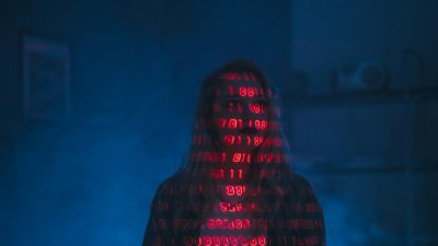 A mysterious silhouette with red binary code projected over the face, set against a dark, moody background.